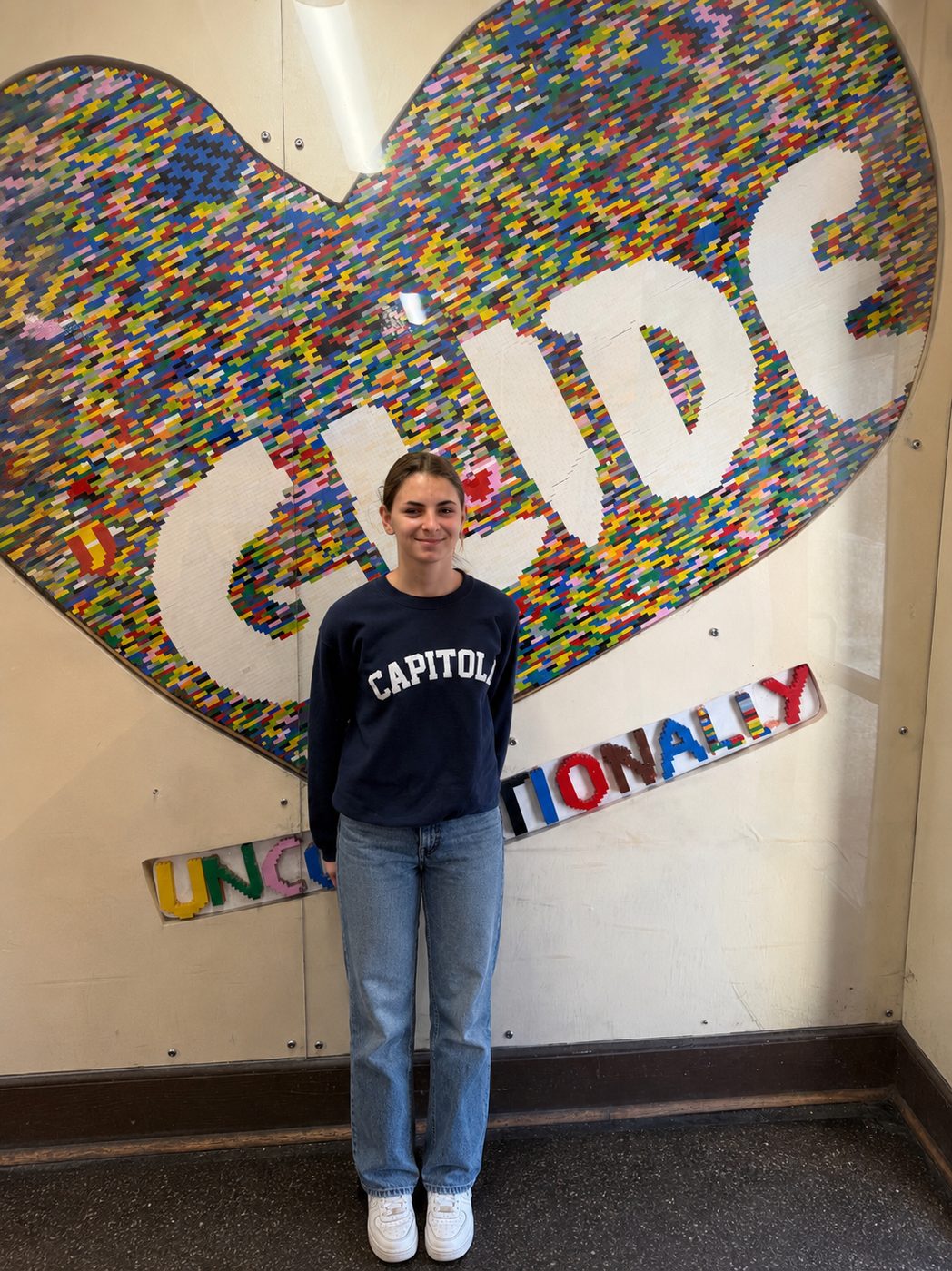 Elia in front of the colorful GLIDE 'Unconditionally' heart mural